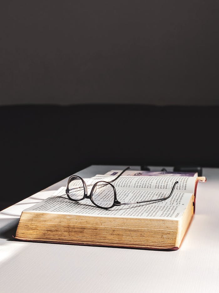 A pair of vintage eyeglasses lying on an open book on a minimalist table, perfect for reading themes.